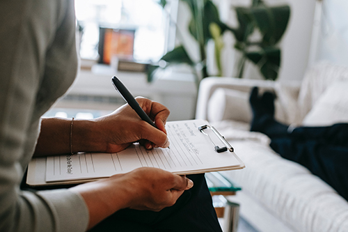 Woman sitting in a chair writing in a notebook with a black pen