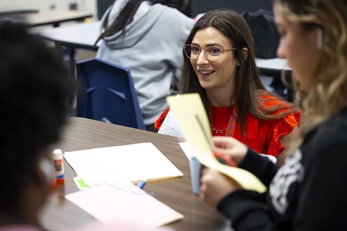 Student sitting at a desk in class with brown hair, glasses and a red shirt