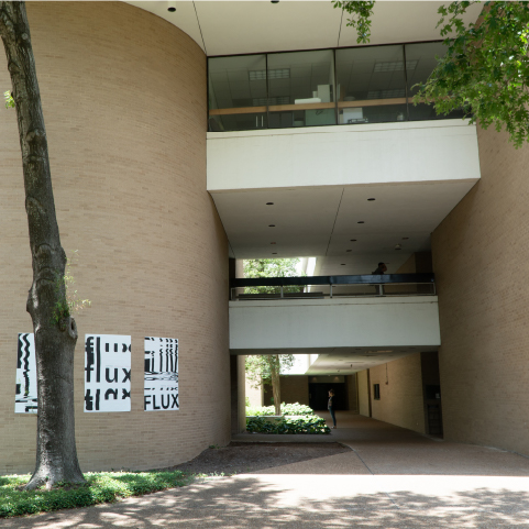 A taupe and cream building with a wide outdoor corridor covered by a second-floor walkway and a third-floor with large windows.