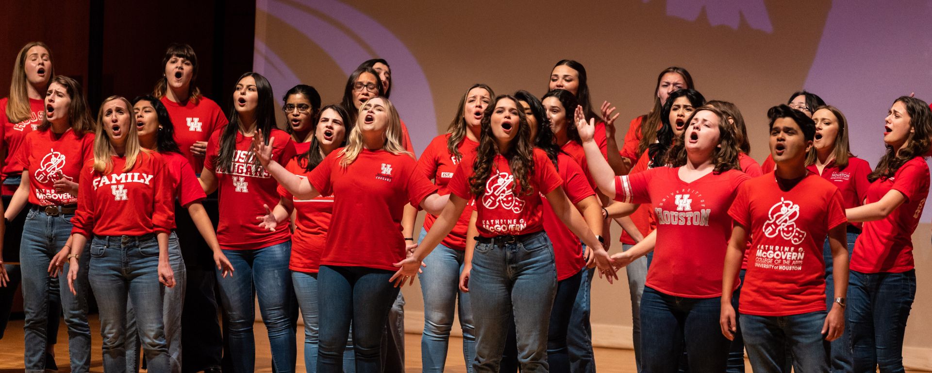 The UH Concert Chorale in red t shirts smiling and singing animatedly