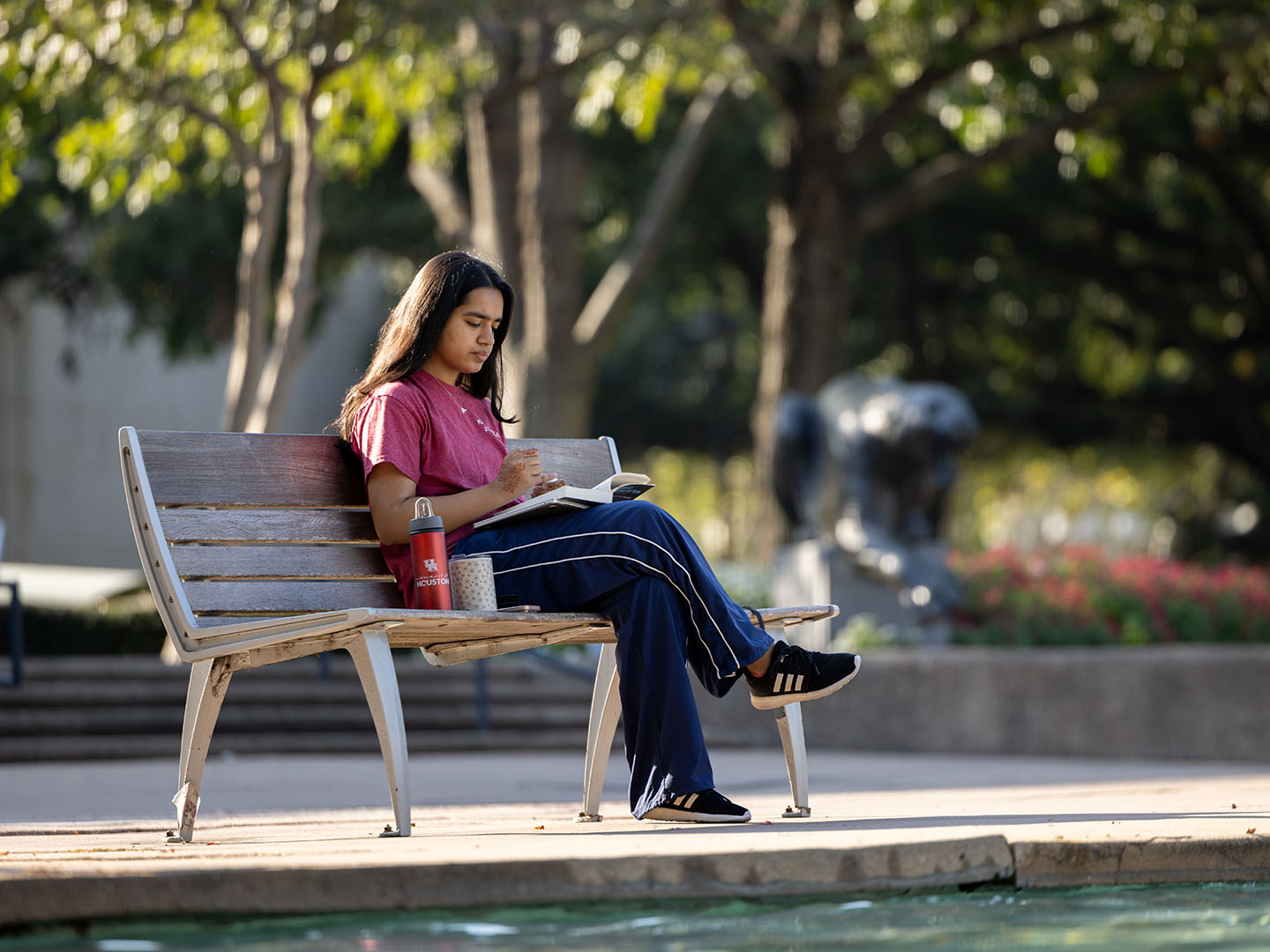 Student reading a book while sitting at bench in Cullen Family Plaza at the University of Houston.