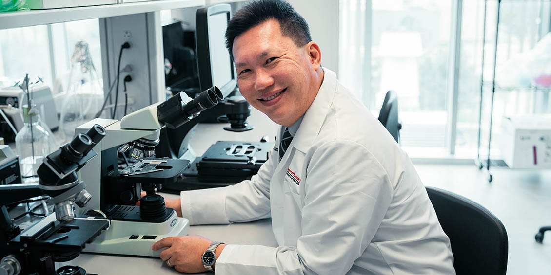 Photo of Tam in his lab in front of a microscope