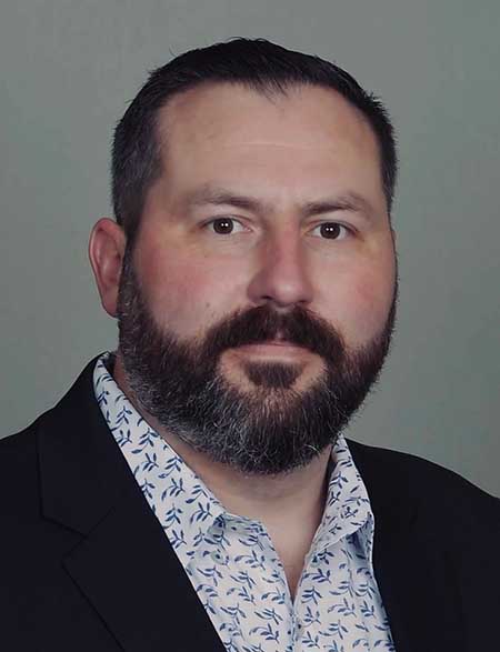 Portrait of a white man with short black hair and a short black and grey beard.