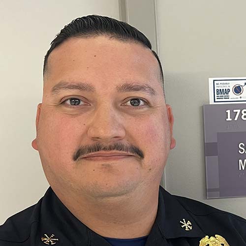 Portrait of a Hispanic man smiling with short hair and a mustache.